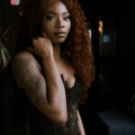 Stylish portrait of a woman in a trendy black outfit, exuding elegance in a dimly lit interior.